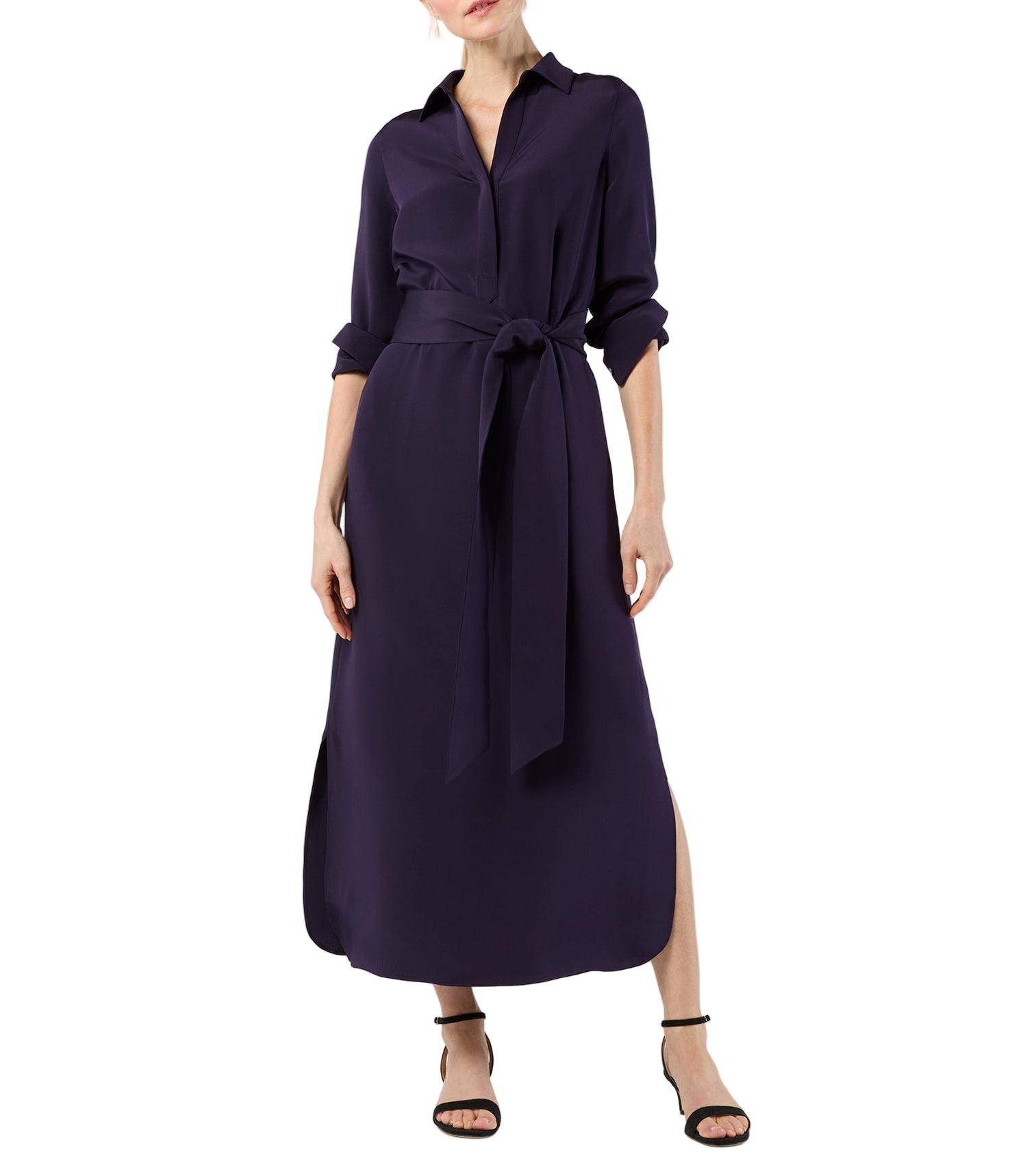 A woman wears the Ann Mashburn Piper Maxi Dress in lightweight dark purple, featuring a collar, belted waist, and side slit, paired with black strappy heels.