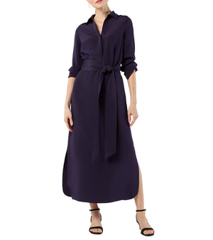 A woman wears the Ann Mashburn Piper Maxi Dress in lightweight dark purple, featuring a collar, belted waist, and side slit, paired with black strappy heels.