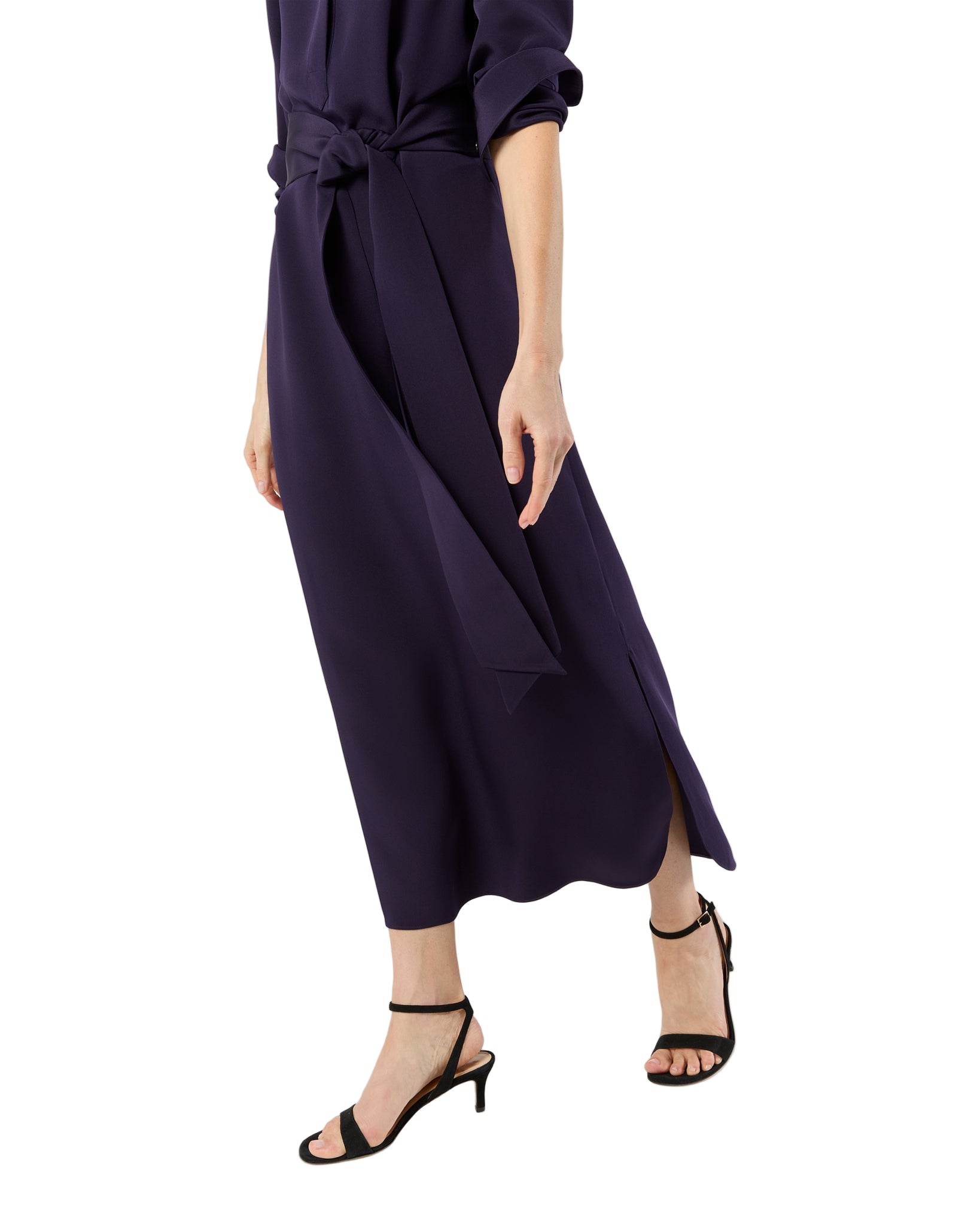 A person walks forward against a white background, wearing Ann Mashburn's long, dark purple Piper Maxi Dress in lightweight crepe de chine with a waist tie and black heeled sandals.