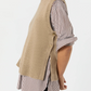 A person models the Ann Mashburn Marion Sweater, a beige cashmere vest, layered over a brown-and-white striped long-sleeve shirt with black pants, shown in profile against a plain background.