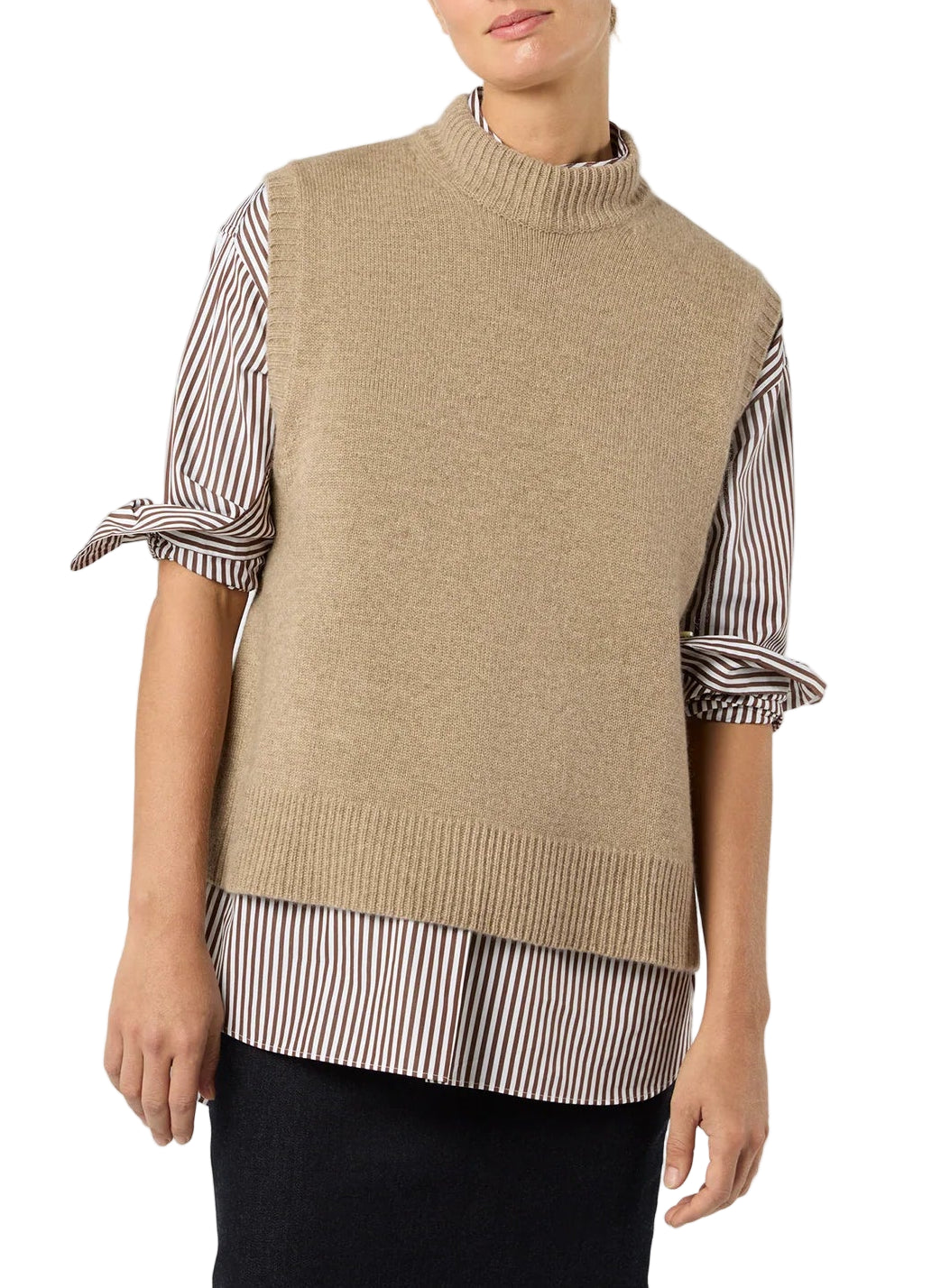 A person wearing the Ann Mashburn Marion Sweater, a beige cashmere sweater vest, layered over a striped button-up shirt with tied sleeves and paired with a black skirt.