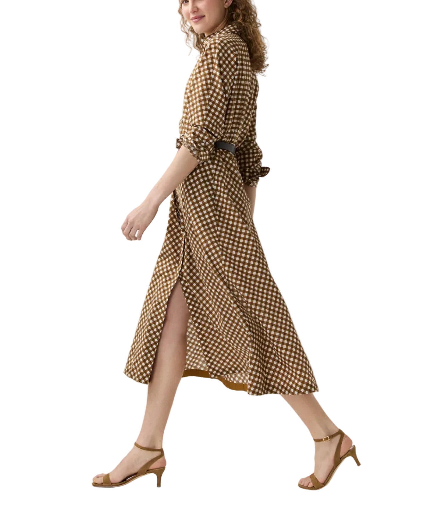 A woman wearing the Ann Mashburn Charlie Shirtwaist Gingham Dress with rolled sleeves and tan heels walks forward against a white background.