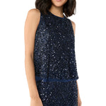 A woman wears the Ann Mashburn Gia Beaded Mesh Shell, a sleeveless, dark blue sequined top, paired with a matching sequined skirt. Her face is partially out of frame.