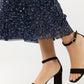 A person wearing the Ann Mashburn Ruby Beaded Mesh Skirt paired with black heeled sandals featuring ankle straps and an open toe design.