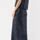 A woman wears the Ann Mashburn Gia Beaded Mesh Shell and matching midi skirt with black ankle-strap block heels, standing against a plain white background.