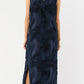 A woman is seen from the back against a white background wearing the Ann Mashburn Susy Shift Maxi Dress in sleeveless navy textured fabric with a side slit, paired with black block-heel sandals.