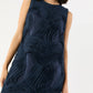 A woman stands against a plain background wearing the Ann Mashburn Susy Shift Maxi Dress, a sleeveless navy blue dress featuring textured, wavy fabric patterns.