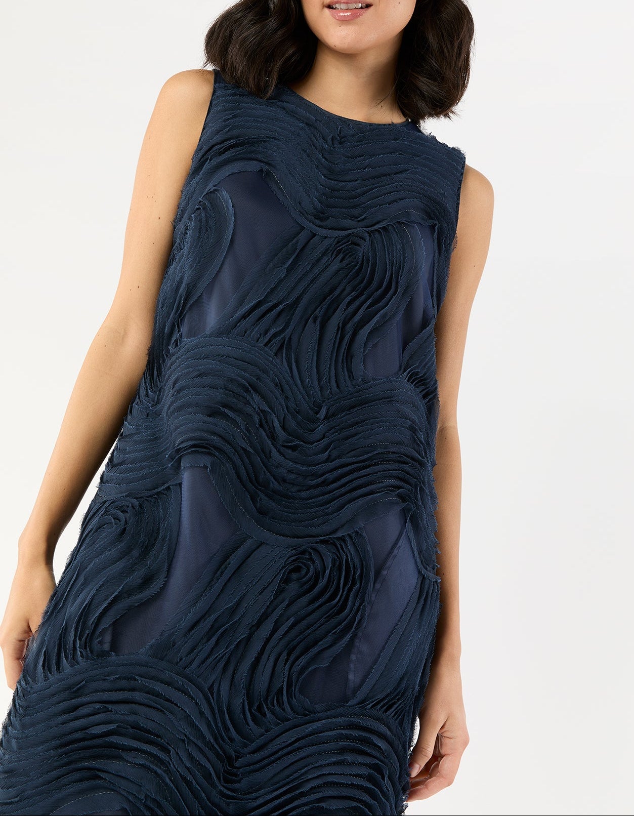 A woman stands against a plain background wearing the Ann Mashburn Susy Shift Maxi Dress, a sleeveless navy blue dress featuring textured, wavy fabric patterns.