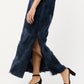 A person wearing the Ann Mashburn Susy Shift Maxi Dress in textured navy blue with a slit and black block-heeled sandals, walking against a plain light background.