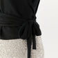 A close-up of a person wearing the Ann Mashburn Mika Cashmere Wrap Sweater in black, tied at the waist, paired with a silver sequin skirt against a plain background.