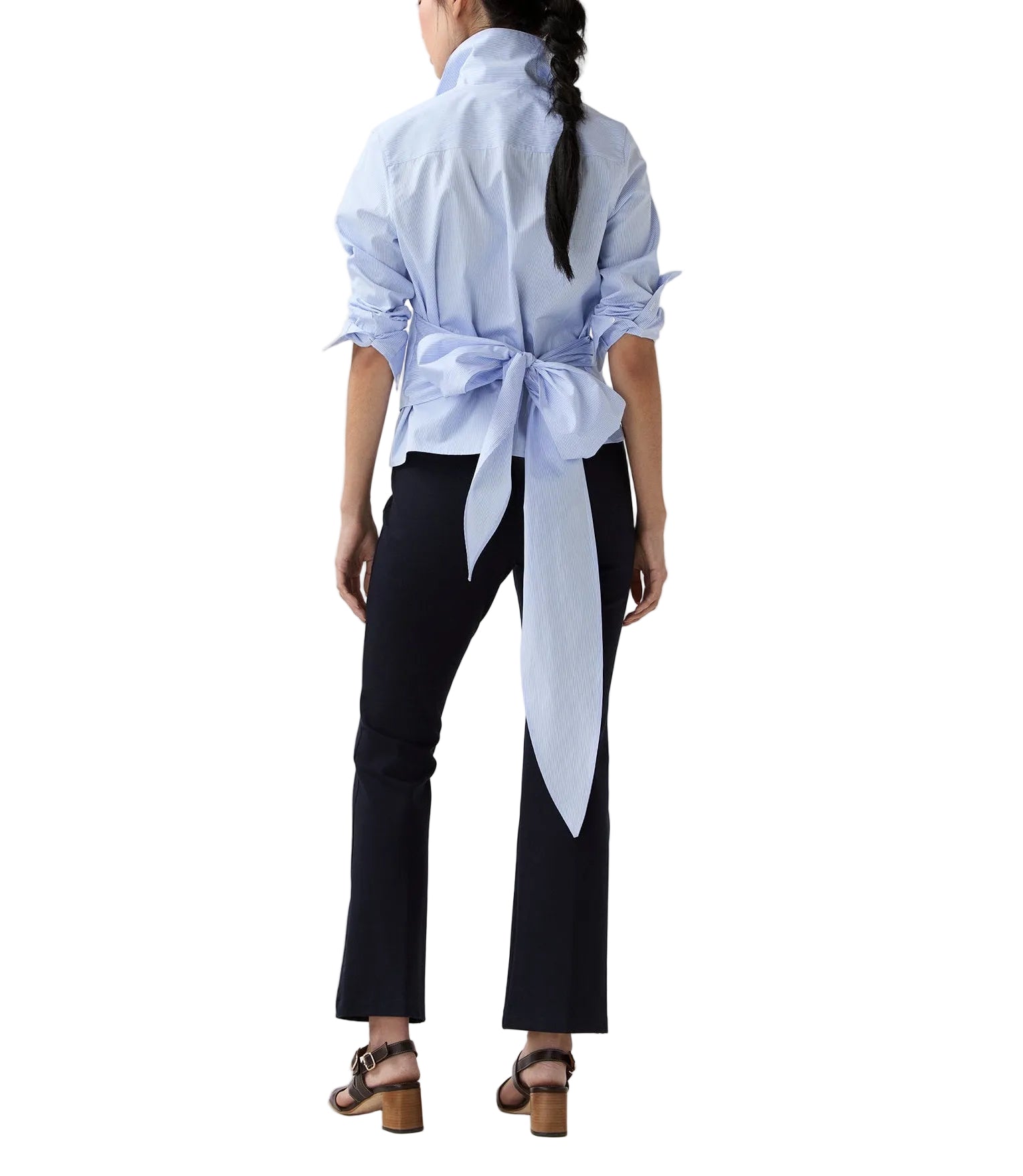 A woman stands facing away, wearing the Ann Mashburn Hilary Wrap Small Bengal Top with a large back bow, paired with black pants and brown heeled sandals.