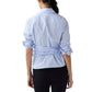 A woman stands with her back to the camera, wearing the Ann Mashburn Hilary Wrap Small Bengal Top—a light blue blouse with tied sleeves and self-tie belt—paired with black pants, on a white background.