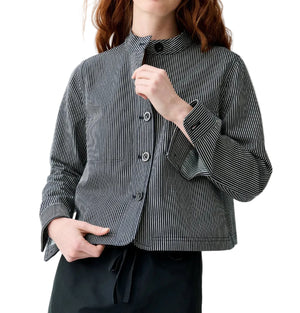 A person wears the Ann Mashburn Short Chore Jacket over a black and white vertically striped button-up shirt with long sleeves and black pants, standing against a white background.