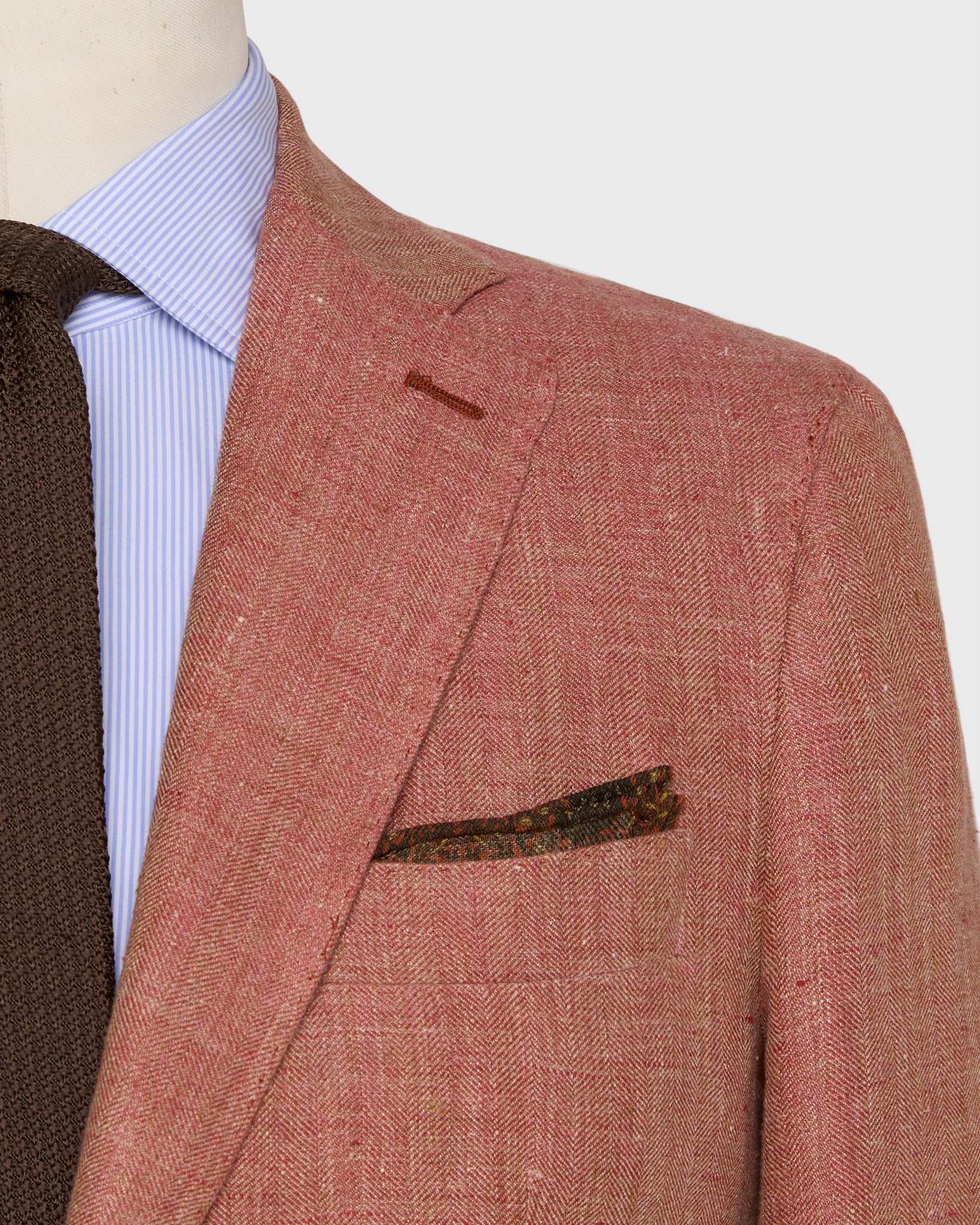 Close-up of a person wearing the Sid Mashburn Kincaid No. 3 Jacket, paired with a light blue striped shirt, brown knitted tie, and a patterned pocket square.