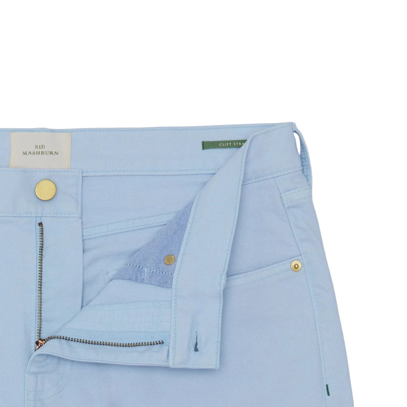 Close-up of Sid Mashburn’s Clift Straight Leg Jean in light blue, garment-dyed finish, featuring five pockets, a partially open zipper fly, visible waistband labels, front pockets, and metallic snap buttons.