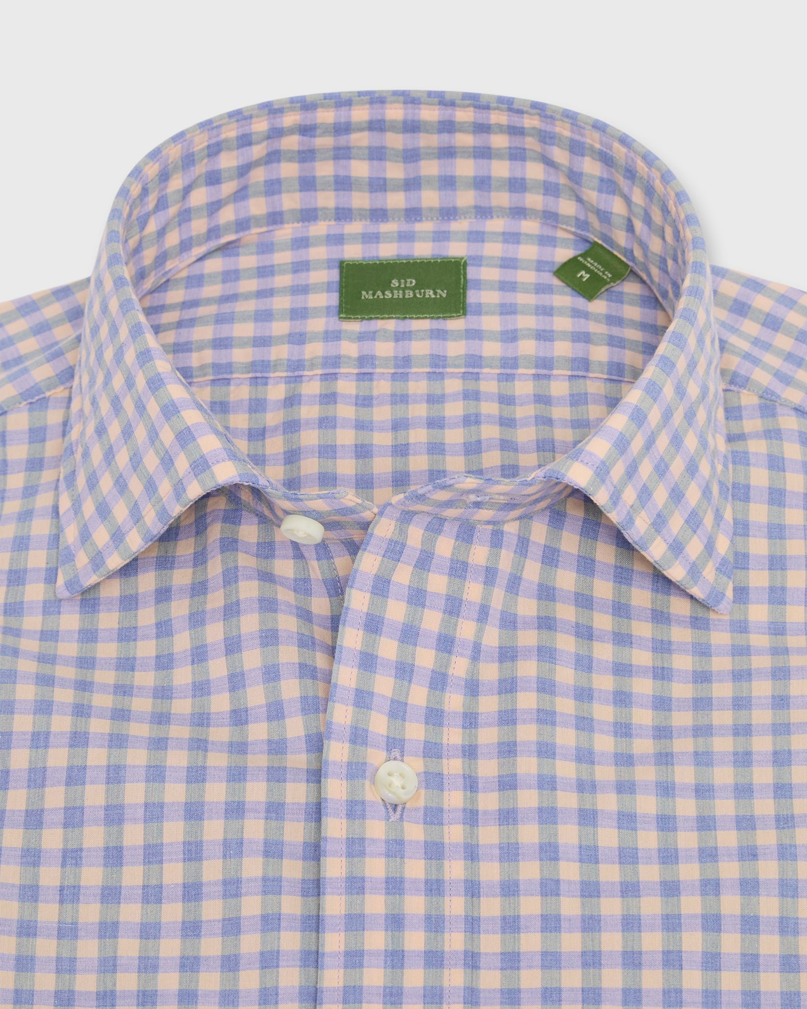 A Sid Mashburn Spread Collar Sport Shirt for men, styled in a peach and blue plaid pattern with a spread collar, is neatly folded to display the Sid Mashburn label inside the collar.