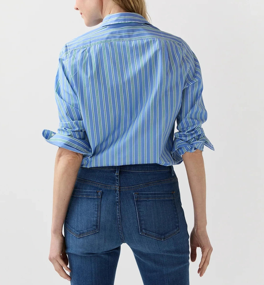 A woman faces away, wearing the Ann Mashburn Sidney Stripe Shirt with a classic spread collar and rolled-up sleeves, paired with blue jeans against a plain light background.
