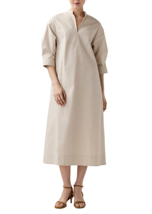 A woman in Ann Mashburn’s Cadie Paperweight Stretch Poplin Dress—loose-fitting with a tuxedo bib, three-quarter sleeves, and V-neckline—paired with brown heeled sandals for a chic, effortless travel look.