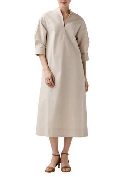 A woman in Ann Mashburn’s Cadie Paperweight Stretch Poplin Dress—loose-fitting with a tuxedo bib, three-quarter sleeves, and V-neckline—paired with brown heeled sandals for a chic, effortless travel look.