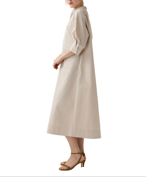 A woman wearing the Ann Mashburn Cadie Paperweight Stretch Poplin Dress in light beige with three-quarter sleeves and tan heeled sandals, standing sideways against a white background.