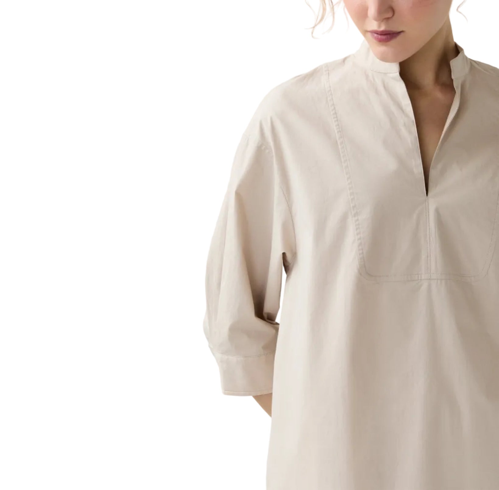 A person is wearing the Ann Mashburn Cadie Paperweight Stretch Poplin Dress, a loose, light beige long-sleeve style with a split neckline, standing against a plain white background.