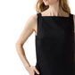 A woman stands with one hand in her pocket against a white background, wearing the Ann Mashburn Rosalind Dress—a sleeveless black poplin style with a square neckline.
