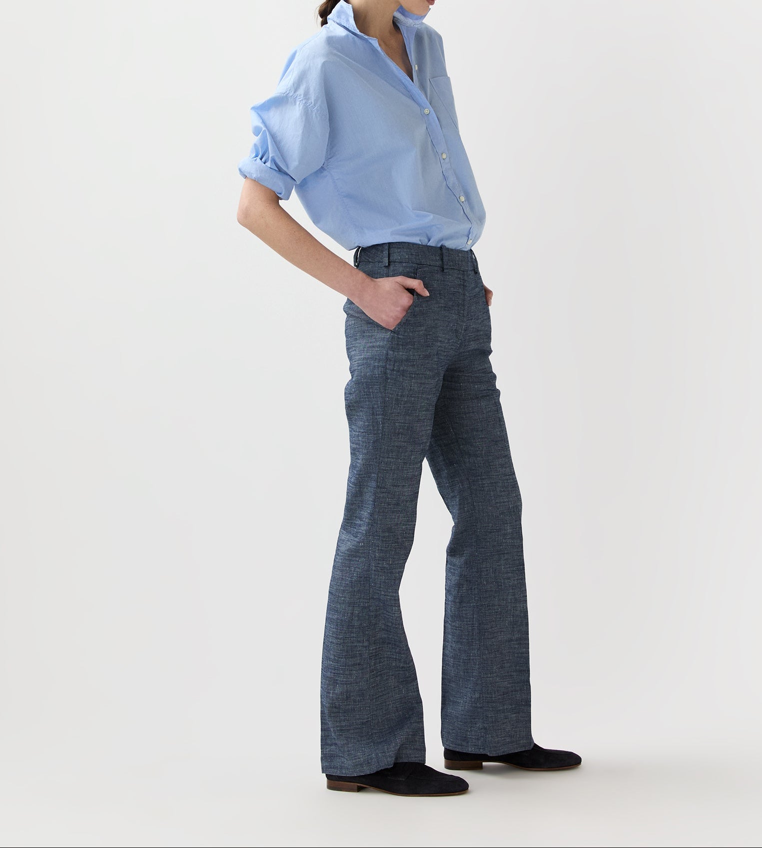Person wearing a light blue button-up shirt with rolled-up sleeves, Ann Mashburn Lane Cotolino Chambray Pant, and black shoes, standing against a plain white background.