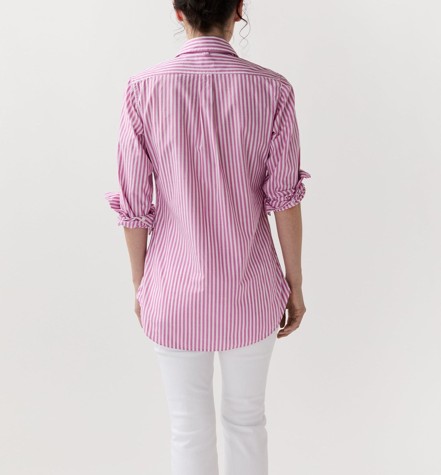 A person faces away, wearing the Ann Mashburn Boyfriend Stripe Chambray Shirt in pink and white, paired with white pants against a plain light background.