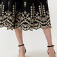 A person in Ann Mashburn's Short-Sleeve Classic Shirtwaist Dress—a black skirt with white floral embroidery near the hem—styled with black ankle-strap sandals for a timeless, feminine look.