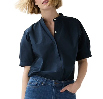 A woman poses against a white background with one hand in her pocket, wearing blue jeans and the Ann Mashburn Perry Poplin Shirt, a navy Italian poplin short-sleeve button-up.