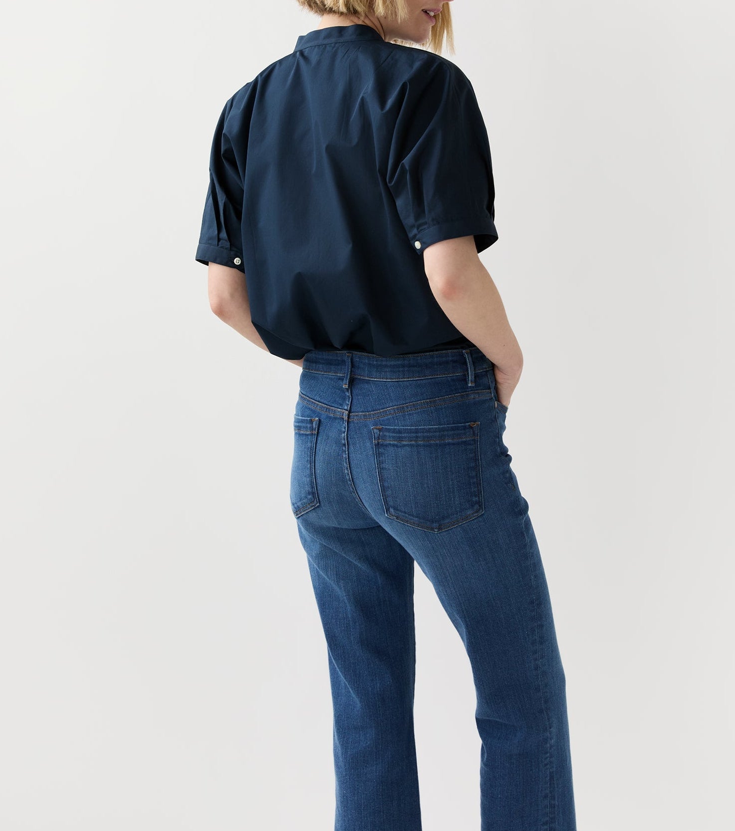 A person stands with their back to the camera, wearing the Ann Mashburn Perry Poplin Shirt in navy with a mandarin collar and blue jeans, set against a plain light background.