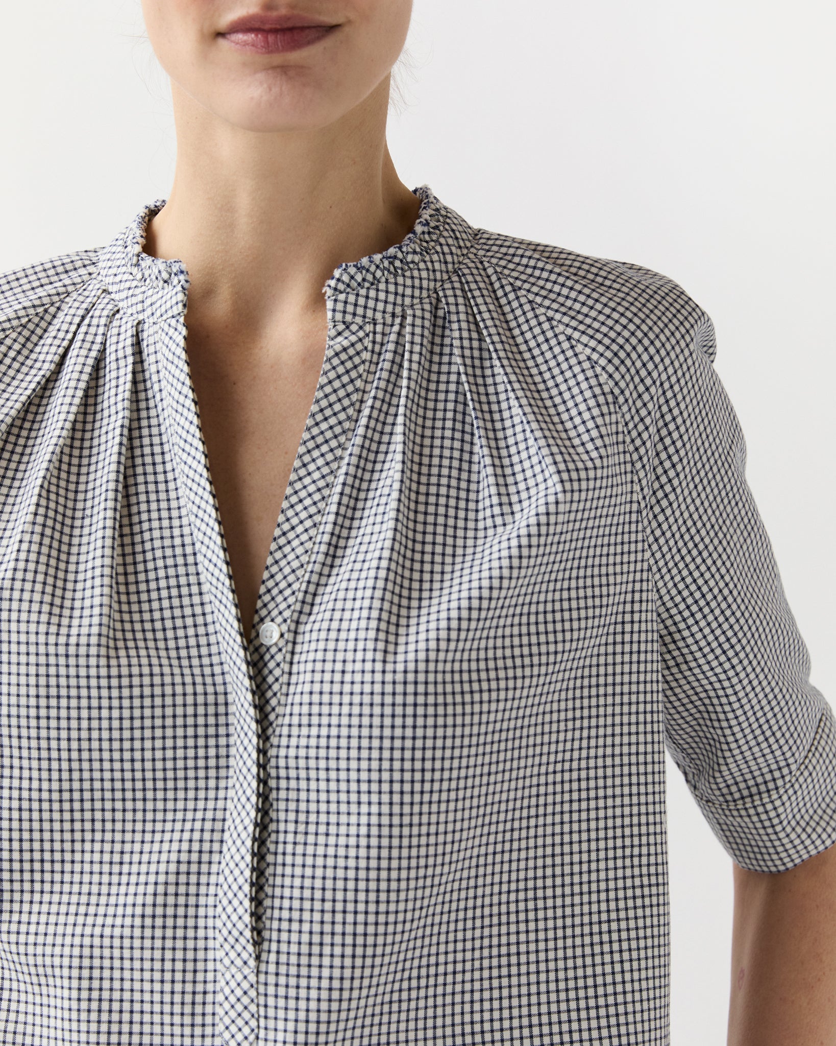 A person wears the Ann Mashburn Sage Blouse, a collared, long-sleeve poplin top with a small black and white check pattern, shown from shoulders to mid-torso against a plain background.