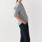 A person stands sideways with one hand in their pocket, wearing the Sage Blouse by Ann Mashburn and dark pants against a plain background.