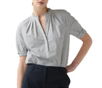 A person wearing the Ann Mashburn Sage Blouse—a black and white checkered Portuguese poplin popover with short sleeves—and dark trousers, standing with one hand in their pocket.
