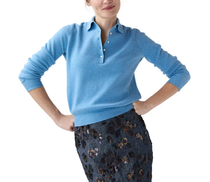 A person wears the Ann Mashburn Connor Cotton/Silk Sweater in light blue, featuring button details, paired with a dark blue floral skirt, standing hands on hips against a white background.