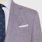 A close-up of a person wearing the Sid Mashburn Kincaid No. 2 Jacket in light purple herringbone cloth, paired with a white dress shirt, navy patterned tie, and a white pocket square.