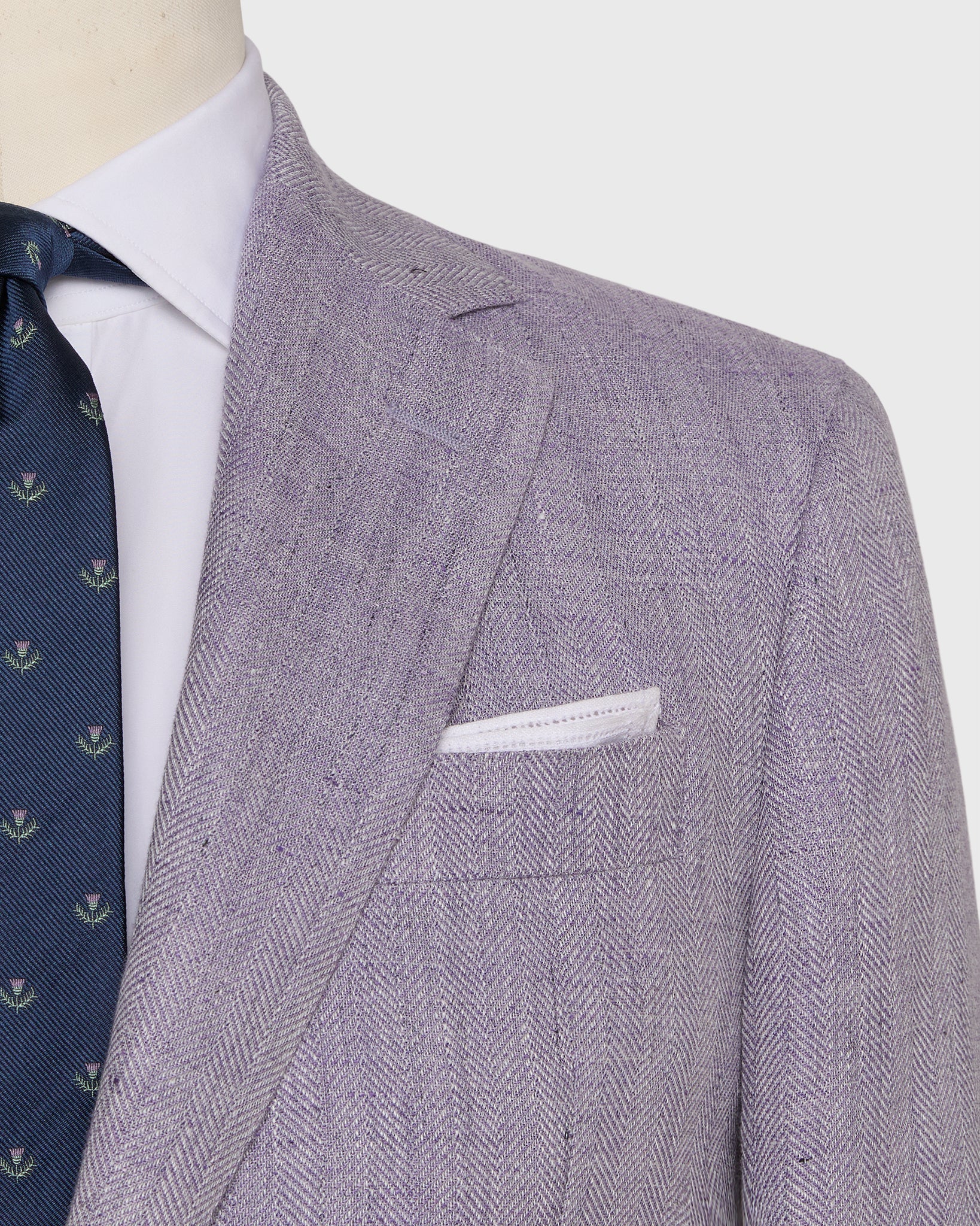 A close-up of a person wearing the Sid Mashburn Kincaid No. 2 Jacket in light purple herringbone cloth, paired with a white dress shirt, navy patterned tie, and a white pocket square.