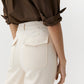 Wearing Ann Mashburn’s Camille Patch-Pocket Stretch Jean, a high-waisted cream-colored style with back flap pockets, paired with a brown rolled-sleeve shirt against a plain background.