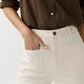 Wearing a brown button-up shirt with rolled sleeves, paired with Ann Mashburn's Camille Patch-Pocket Stretch Jean, one hand casually placed in a front pocket.