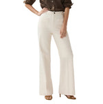 A person wears a brown long-sleeve shirt, Ann Mashburn Camille Patch-Pocket Stretch Jeans in cream, and tan heeled sandals, standing with one hand on their hip against a white background.