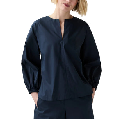 Someone wearing the Ann Mashburn Meghan Top, a dressy nylon blouson with a split neckline, paired with matching wide leg pants and standing with hands in pockets.