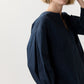 A person with short blonde hair wears the loose-fitting, long-sleeve Meghan Top by Ann Mashburn. Their face is partially out of frame against a plain light background.