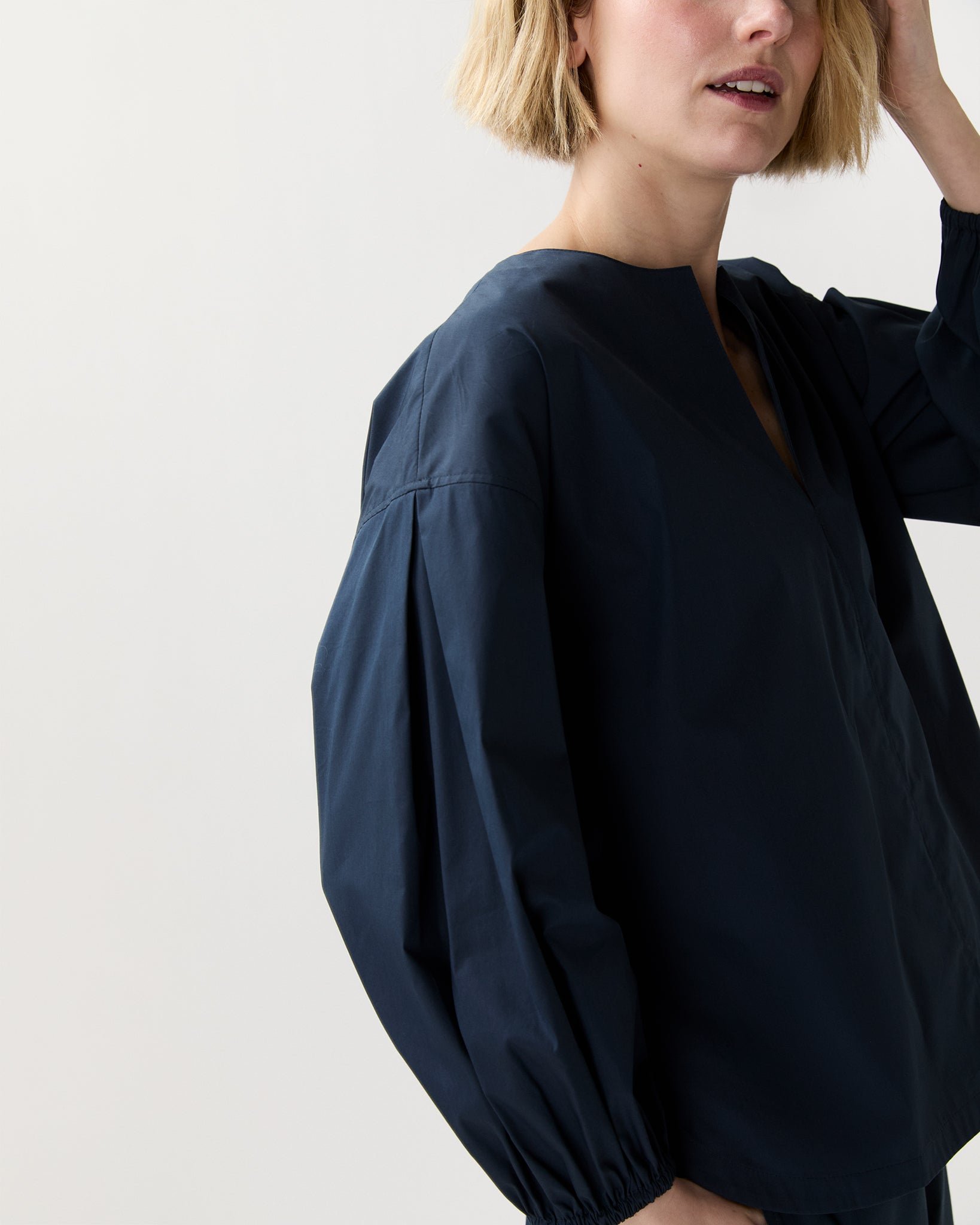 A person with short blonde hair wears the loose-fitting, long-sleeve Meghan Top by Ann Mashburn. Their face is partially out of frame against a plain light background.
