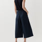 A person faces away, wearing a sleeveless black blouson top, Ann Mashburn Drew Pant in navy poplin, and tan heeled sandals against a plain light background.