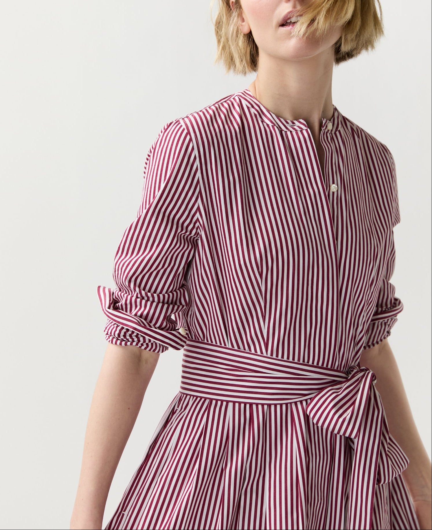 A person wearing the Ann Mashburn Felicity Shirtwaist Dress featuring red-and-white vertical stripes and a waist tie, standing against a plain light background.
