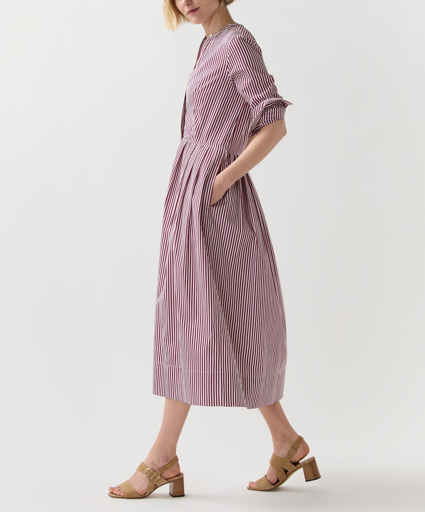 A person wearing the Ann Mashburn Felicity Shirtwaist Dress—long-sleeved, red and white striped with pockets—and tan heeled sandals, standing against a plain white background.
