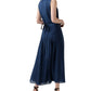 A woman wears the Ann Mashburn Rose Dress—an ankle-length, sleeveless navy pleated dress with a square neckline and tie-back—paired with black heeled sandals, ideal for elegant evening occasions.