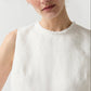 A person is shown from the shoulders up against a plain background, wearing the Ann Mashburn Mimi Linen Top—a sleeveless white Belgian linen shell with a frayed neckline.