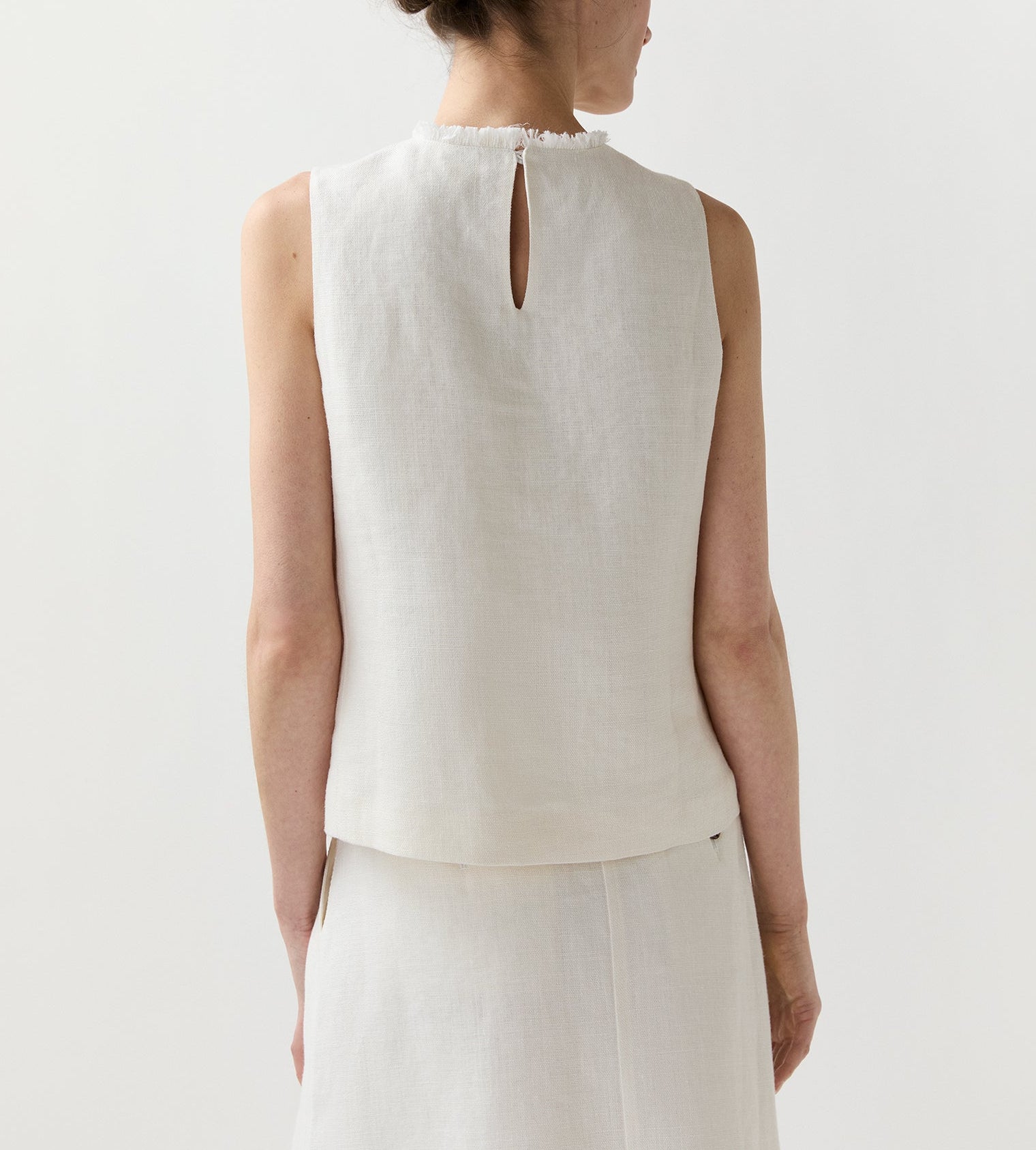 A woman, shown from behind, wears the Ann Mashburn Mimi Linen Top—a sleeveless shell in off-white Belgian linen with a small back keyhole—paired with a matching skirt.