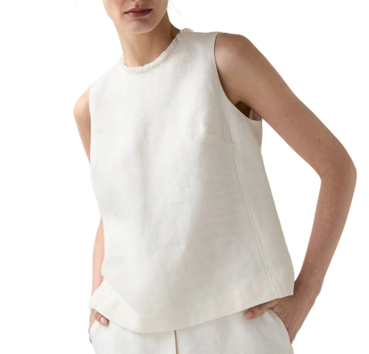 A person wears the Ann Mashburn Mimi Linen Top, a sleeveless, off-white Belgian linen shell with a high neck and relaxed fit, paired with matching light pants and hands in pockets.